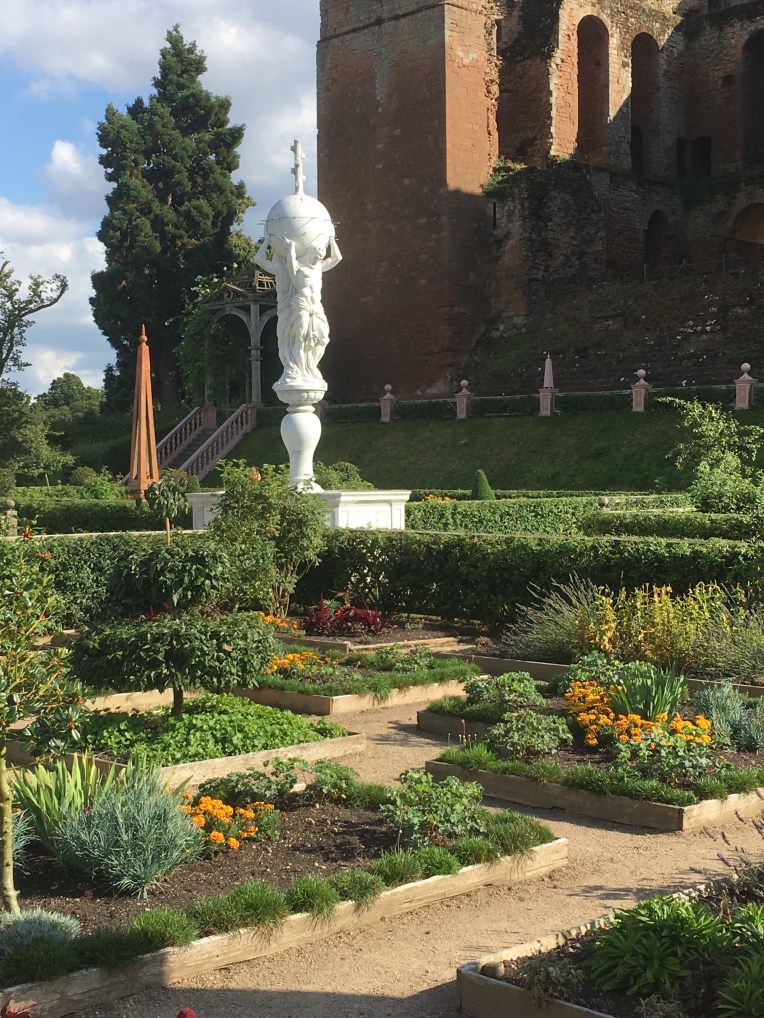 An Elizabethan garden scene at Kenilworth Castle, with a small garden area featuring raised beds, topiary and the Atlas fountain.